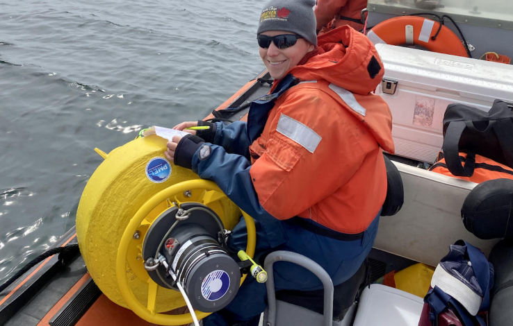 Grey skys with Angie in a beanie and orange life jacket sitting next to a yellow buoy on a rigid inflatable boat