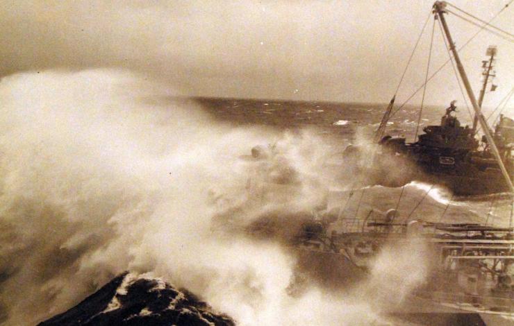 Sepia image of a ship and a destroyer encountering a large wave sweeping past the oiler's bow