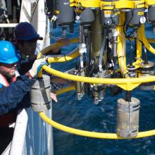 Two men who hard hats pull in a CTD rosette from the ocean. 