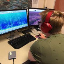 A master's student sitting in front of a computer looking at sound spectrogram on a computer from 