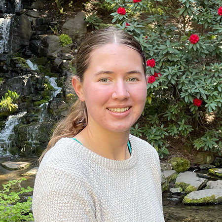 Eleanor in front of small rocky waterfall and stream and bushes with red flowers