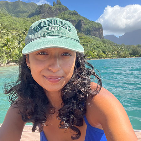 Nishita in front of teal water and sunny, vegetation-covered mountains